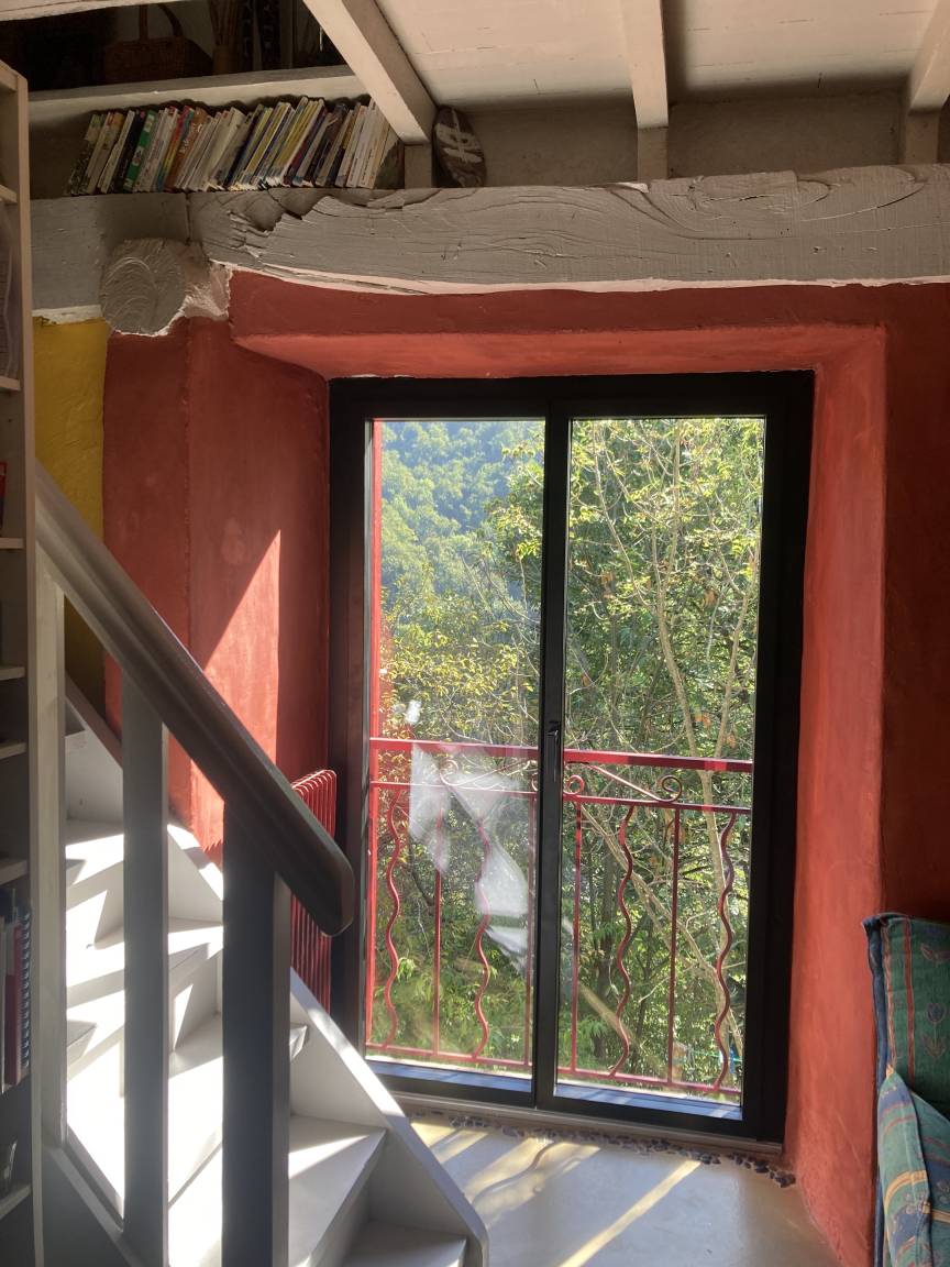 Une porte-fenêtre encadrée de murs terracotta, ouverte sur le versant boisé