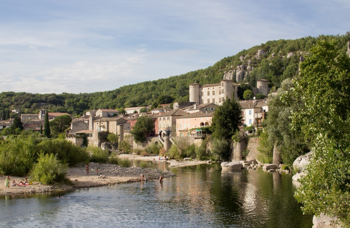 Le château de Vogüé dominant le village et l'Ardèche, où les baigneurs profitent de la rivière